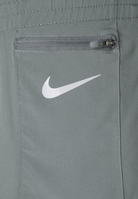 Pantalones cortos de Nike en un tejido gris claro que cuentan con un bolsillo con cremallera y un logo reflectante blanco. La textura parece suave con un acabado mate.