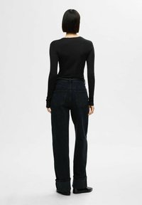 Svart långärmad topp i kombination med mörka denimbyxor i hög midja. Byxorna har vida ben och vikta muddar, vilket ger en avslappnad look.