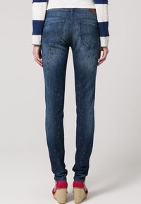 Smal blå denimjeans med stjärnmönster, fem fickor och ljus blekning. Smal design och kontrasterande sömmar. Bärs med klacksandaler.