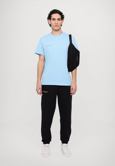 Svijetloplavi T-shirt, crni trenirka, crna torba na rame, bijele tenisice; jednostavan dizajn, opušteni kroj, tekstualni detalji na majici, glatka tkanina.