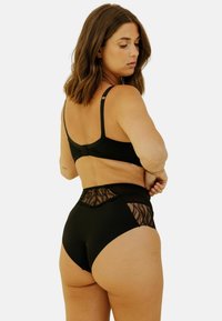 Soutien-gorge sans fil noir avec bretelles ajustables et culotte taille haute assortie, présentant des détails en dentelle transparente au dos et sur les côtés.
