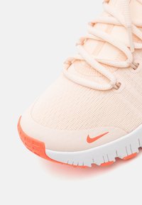 Baskets de sport couleur pêche clair avec une tige en tissu texturé, des lacets ton sur ton et des accents orange, dotées d'une semelle extérieure blanche avec un motif de relief.