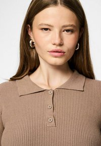 Top de punto acanalado marrón con cuello tipo polo y cierre de tres botones. Textura suave con sutiles detalles de costura.