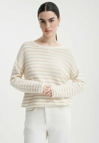 Maglione a manica lunga a righe in crema e beige chiaro, caratterizzato da una vestibilità ampia, scollatura larga e polsi a coste, abbinato a pantaloni bianchi.
