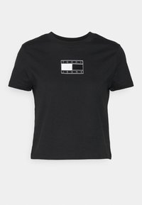 Černé zkrácené tričko vyrobené z bavlny, s bílým obdélníkovým logem se textem "TOMMY JEANS". Krátké rukávy a klasický kulatý výstřih.