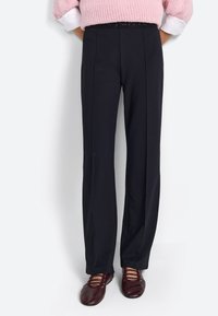 Pantalones negros de corte recto, con pliegues frontales, una textura suave y una cinturilla estrecha. Combinados con zapatos burdeos.