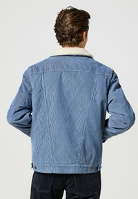 Jeanjacka i ljusblått med en shearlingkrage. Har en klassisk passform, synliga sömmar och knappenvändningar vid fållen.