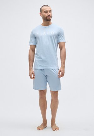 Camiseta de algodón azul claro con la palabra "TIRED" impresa en blanco, combinada con pantalones cortos a juego, ambos con un ajuste relajado y textura suave.