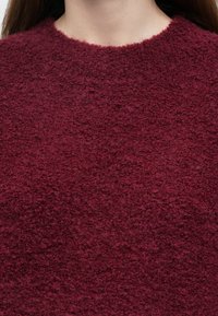 Camisola bordeaux feita de tecido texturizado com um aspeto macio e felpudo. Apresenta um decote redondo e um ajuste descontraído.