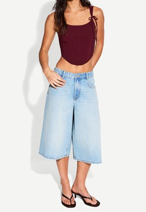 Top court bordeaux avec des liens aux épaules, associé à des culottes en denim large bleu clair et des tongs noires. Tissu doux et coupe décontractée.