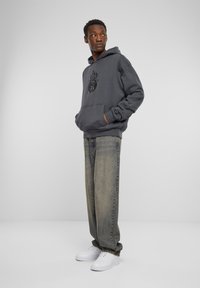 Donkergrijze hoodie met een vlamgrafiek, voorzak en omgeslagen mouwen, gecombineerd met losse lichtgewassen jeans en witte sneakers.