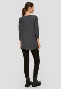 Haut gris texturé à manches longues avec un ourlet arrondi, associé à un pantalon noir ajusté et des bottines noires.