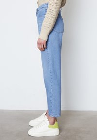 Světle modré džíny s vysokým pasem a rovnými nohavicemi, obsahující pět kapes a jemně vymytou texturu. V kombinaci s bílými teniskami s zelenými akcenty.