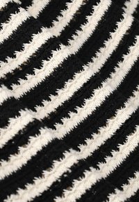 Tissu à rayures noir et blanc présentant des bandes texturées aux bords effilochés, créant un motif de couleurs et de textures alternées.