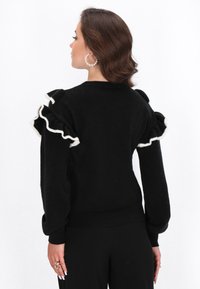 Maglione nero con maniche arricciate e finitura bianca, realizzato in un materiale morbido. Scollo rotondo e design a vita aderente.
