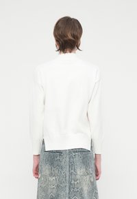 Suéter branco de malha com um decote alto, ombros caídos e punhos e barra canelados, combinado com uma saia texturizada com padrão de cobra azul.
