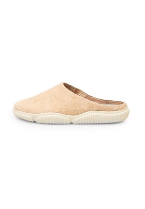 Beige slip-on shoes with a soft, textured upper and white rubber sole featuring a ridged pattern for grip. Rounded toe and backless design.