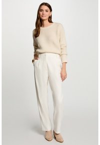 Cremige Strickpullover mit strukturiertem Muster, kombiniert mit hochtaillierten weißen Hosen. Braune Knöchelstiefel runden das Outfit ab.