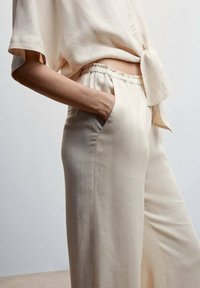 Haut beige en lin à manches courtes avec un détail nœud, associé à un pantalon beige taille haute à jambes larges avec poches latérales.