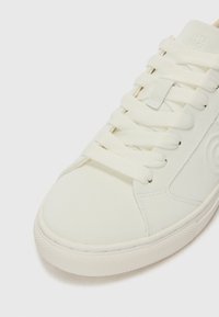 Sneaker bianco con una texture liscia e opaca, caratterizzato da pannelli sovrapposti, cuciture tono su tono e lacci in cotone piatti. Punta arrotondata e suola in gomma.