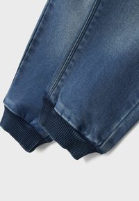 Joggers de denim en azul oscuro con una cinturilla suave y elástica y puños acanalados en los tobillos. La tela presenta una sutil textura desvanecida.