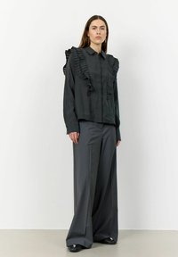 Dark blouse with ruffled accents on shoulders, paired with wide-leg gray trousers. Both items feature a smooth texture and tailored fit.