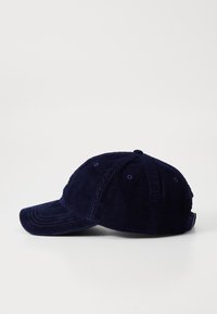 Gorra de béisbol de pana en color azul marino con visera curvada, superficie texturizada y diseño de seis paneles, con etiqueta trasera ajustable.