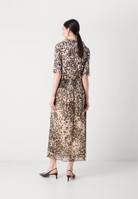 Robe maxi à imprimé léopard avec des manches courtes, de longueur midi, taille élastique et tissu semi-transparent. Portée avec des sandales à talons noires.