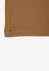 Hnědá texturovaná látka s tkaným vzorem, má rovný okraj s malým rozparkem a prošitou ozdobnou linkou podél spodní části.