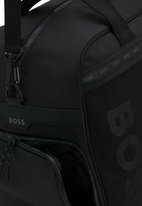 Borsa a duffel nera in materiale nylon testurizzato, con dettagli in rete, hardware argento e logo del brand in rilievo. Presenta una tasca con zip e una tracolla regolabile.