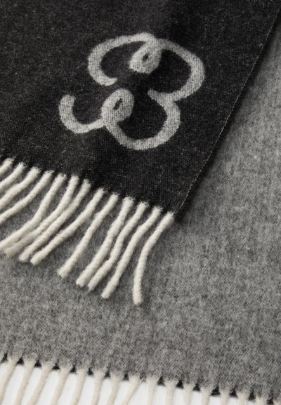 Grå og sort uldsjaal med et stort lys gråt emblem, frynsede kanter og en blød tekstur.