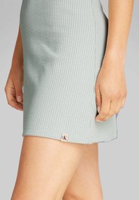 Minigonna azzurro chiaro con un motivo testurizzato simile a una rete. Presenta un'etichetta con logo discreta sull'orlo e una finitura pulita e sartoriale.