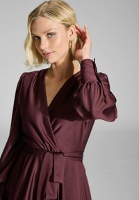 Robe portefeuille bordeaux en tissu lisse avec de longues manches bouffantes et une taille nouée. Elle présente un profond décolleté en V et un design élégant.