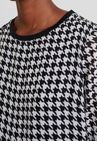 Top in pattern houndstooth bianco e nero con scollatura rotonda e maniche corte, realizzato in un tessuto morbido e leggero.