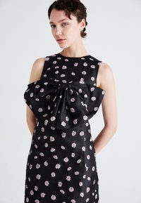 Black dress with pink floral pattern, satin texture, and a large bow detail on the bodice. Sleeveless design with a fitted silhouette.
