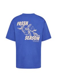 Blå bomullst-shirt med ett grafiskt tryck på baksidan med texten "FRESH SEASON", fotbollar och blad i ljusa färger.