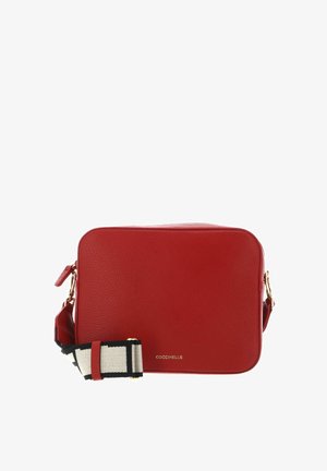 Sac bandoulière rectangulaire en cuir rouge avec ferrures dorées et bandoulière tissée réglable noire et blanche, nom de la marque embossé à l'avant.