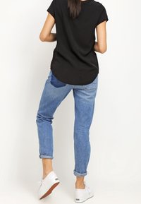 Top nero a maniche corte abbinato a jeans blu chiaro con risvolto e sneakers bianche. L'insieme presenta una vestibilità casual e rilassata.