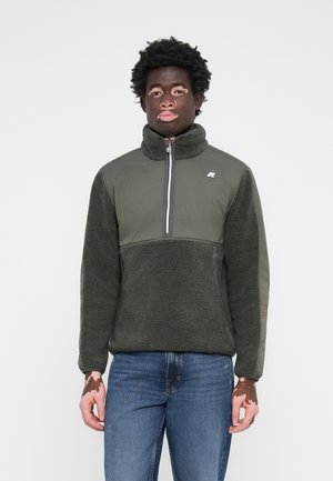 Pullover in pile verde scuro con colletto alto, zip a metà e corpo testurizzato. Accentuato con un tessuto liscio su maniche e dettaglio del logo.
