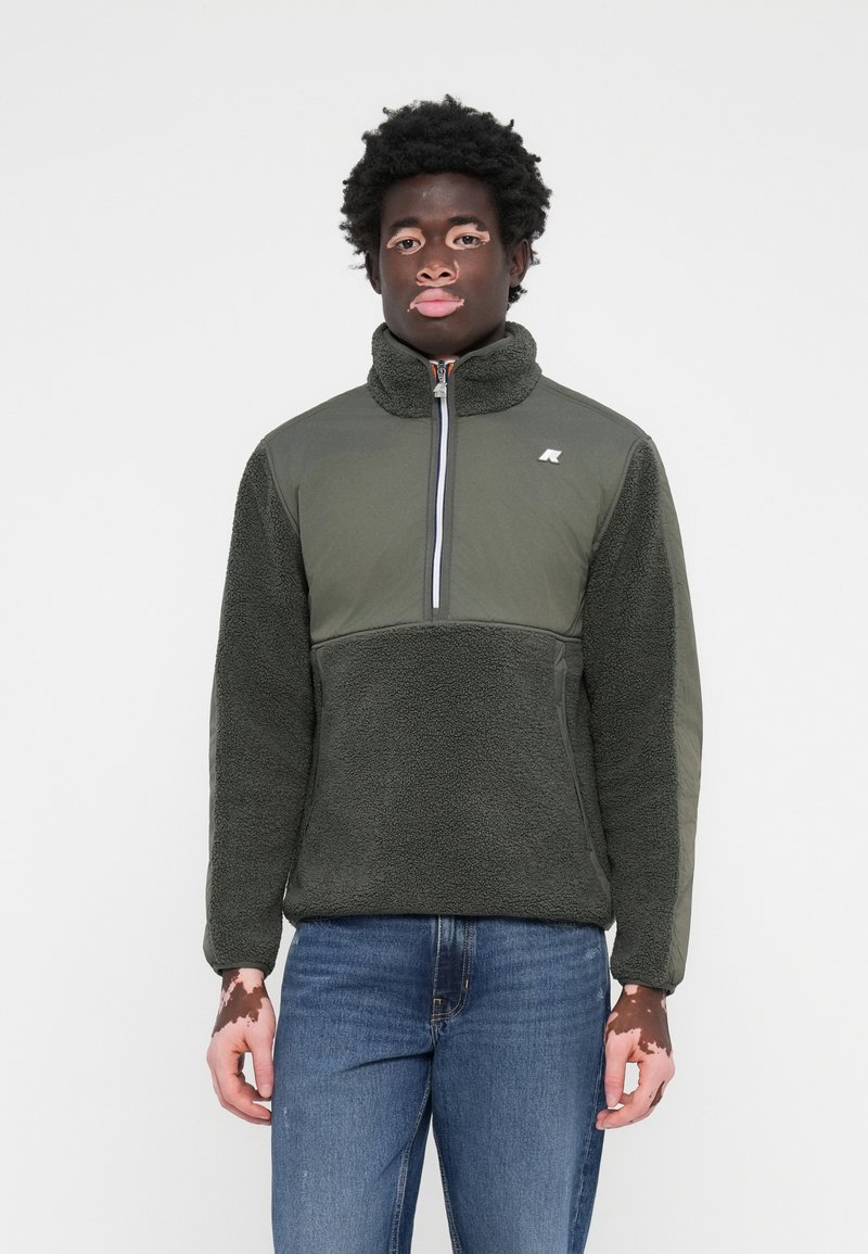Fleece pullover in dark green with a high collar, half-zip, and textured body. Accented with a smooth fabric on sleeves and logo detail.