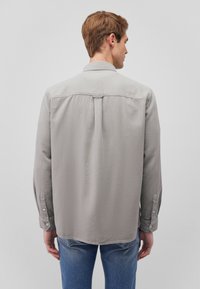 Gray long-sleeve shirt with a pointed collar, button cuffs, and back pleat detail. Made from lightweight fabric with a subtle texture.