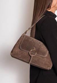 Bruine suède handtas met een rechthoekige vorm, gouden hardware en een ronde bijpassende accent. Voorzien van een zijriem voor het dragen.