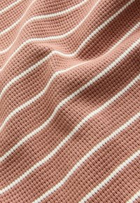 Texturerad tyg i dammig ros med horisontella vita ränder. Materialet har ett vävt mönster som ger en mjuk och mysig känsla.