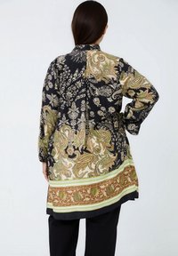 Lange zwarte blouse met ingewikkelde paisley- en bloemenpatronen in goud, groen en beige, met een contrasterende zoomdetail en een geknoopte taille.