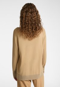 Maglione lavorato a maglia beige con una vestibilità rilassata, caratterizzato da polsini e orlo a coste. Texture morbida, maniche lunghe e design minimalista senza decorazioni.