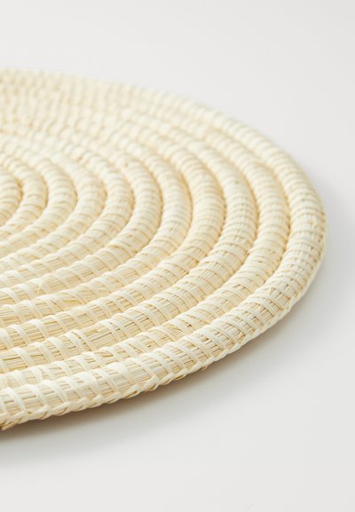 Round, woven placemat made of natural fiber, featuring a light beige color with a textured surface and circular pattern.