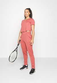 Conjunto desportivo cor-de-rosa composto por uma t-shirt cropped e calças ajustadas, ambos em um tecido suave. Ténis pretos e uma raquete de ténis incluídos.