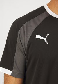 Sort sportsvintertrøje med grå mesh-paneler, hvid krave og hvid Puma-logo. Har korte ærmer og en åndbar stoftekstur.