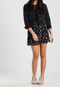 Giacca di jeans nera sopra un vestito floreale nero, con un corpetto aderente e gonna a campana. Indossato con stivali alla caviglia beige chiaro.