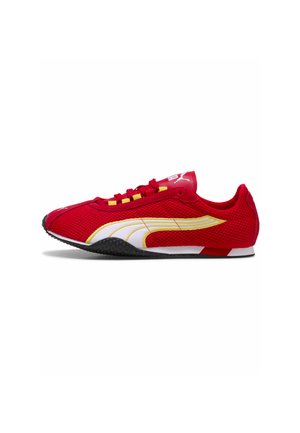 Roter Puma Sportschuh mit weißem und gelbem Logo, schwarzer Sohle, roten Schnürsenkeln und Obermaterial aus Mesh-Stoff, seitlich auf weißem Hintergrund betrachtet.